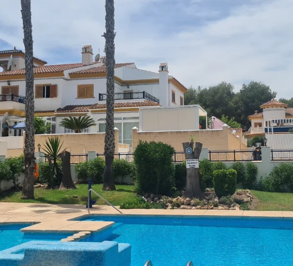 Poolanlage mit Palmen und weißen Häusern unter blauem Himmel