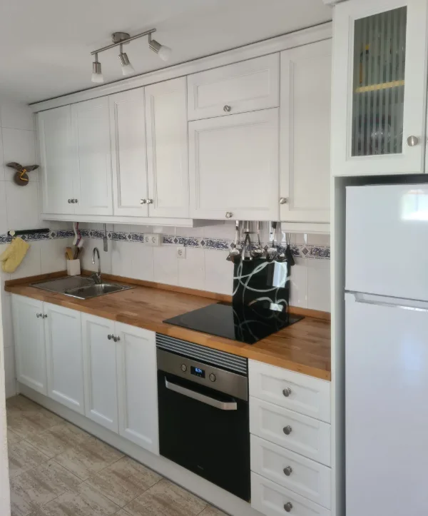 Weiße Küche mit Holzarbeitsplatte, Ceranfeld, Backofen und Kühlschrank