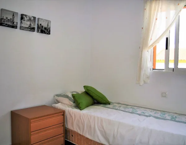 Einzelbett mit grünen Kissen, Kommode und Bilderrahmen an der Wand
