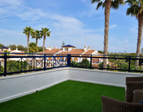 Terrasse mit Kunstrasen und Geländer, Blick über rote Ziegeldächer und Palmen