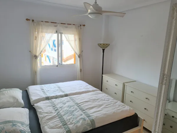 Doppelbett mit Kommode und Deckenventilator vor einem Fenster