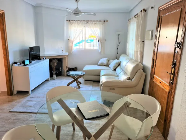 Helles Wohnzimmer mit Sofa, Sesseln, Fernseher und Deckenventilator
